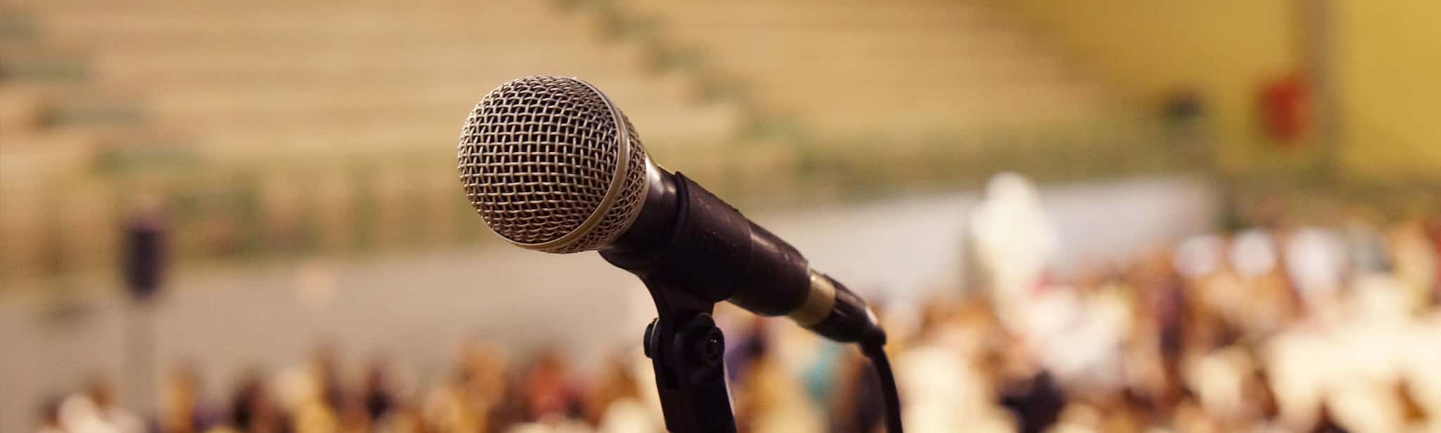 Close-up eines Mikrofons mit einer Personenmenge im Hintergrund in Tiefenunschärfe.